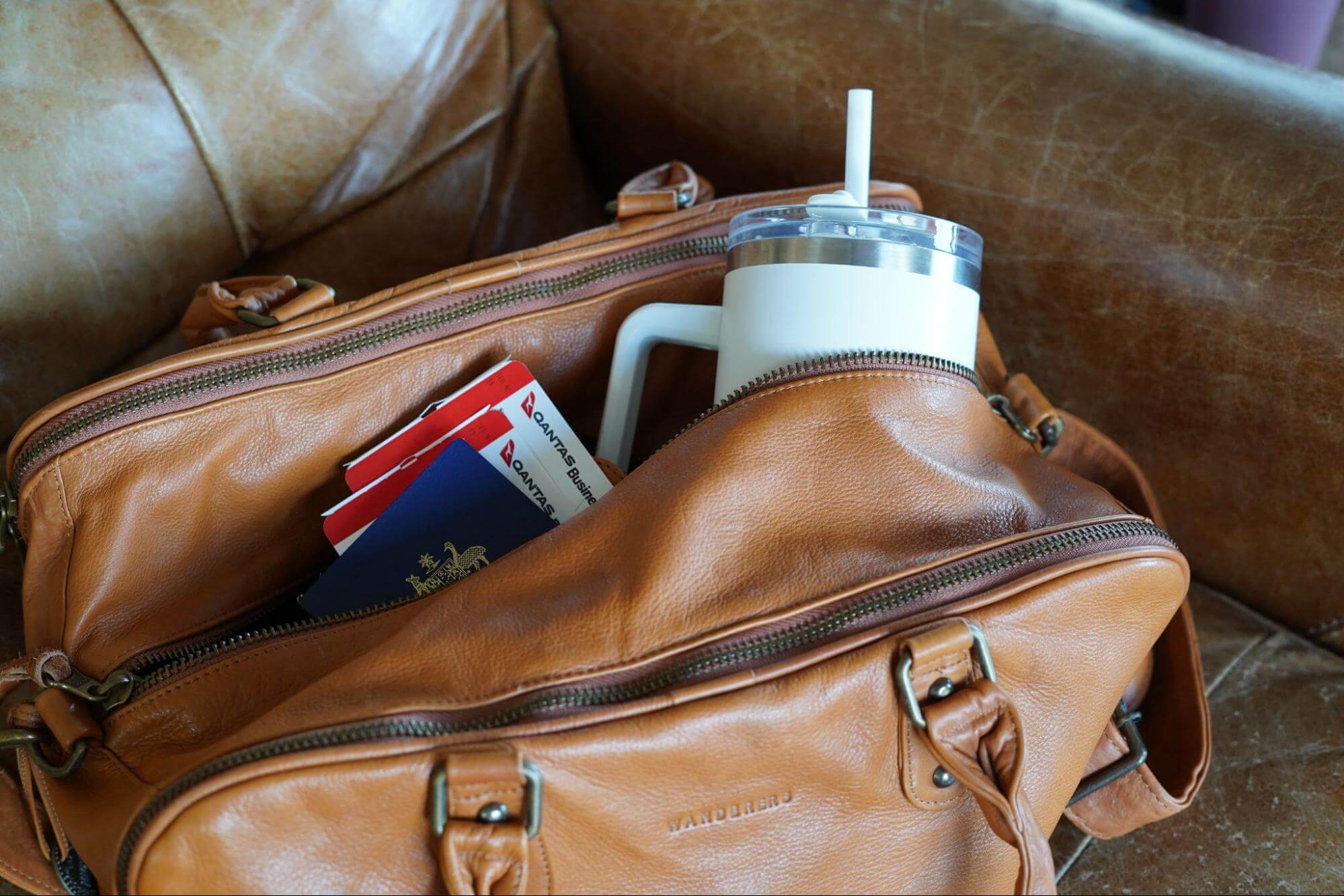 Reusable water bottle tickets and passports in travel bag on couch