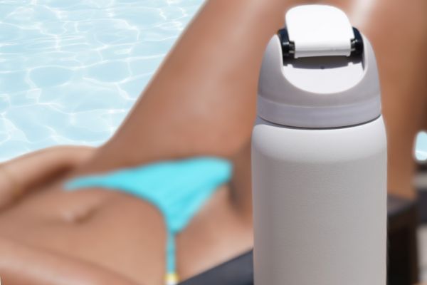 White Owala reusable water bottle containing Access Filter Straw in front of tanned female with aqua bikini in front of pool