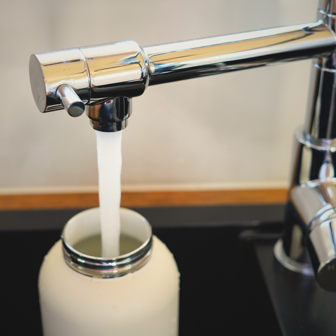 Reusable water bottle being filled with tap water from kitchen sink tap