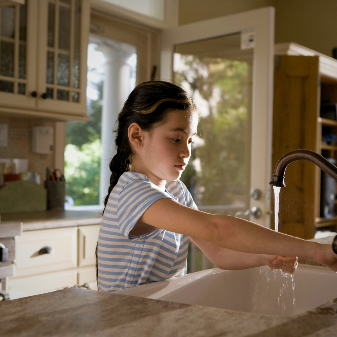 Girl at kitchen sink washing hands in tap water