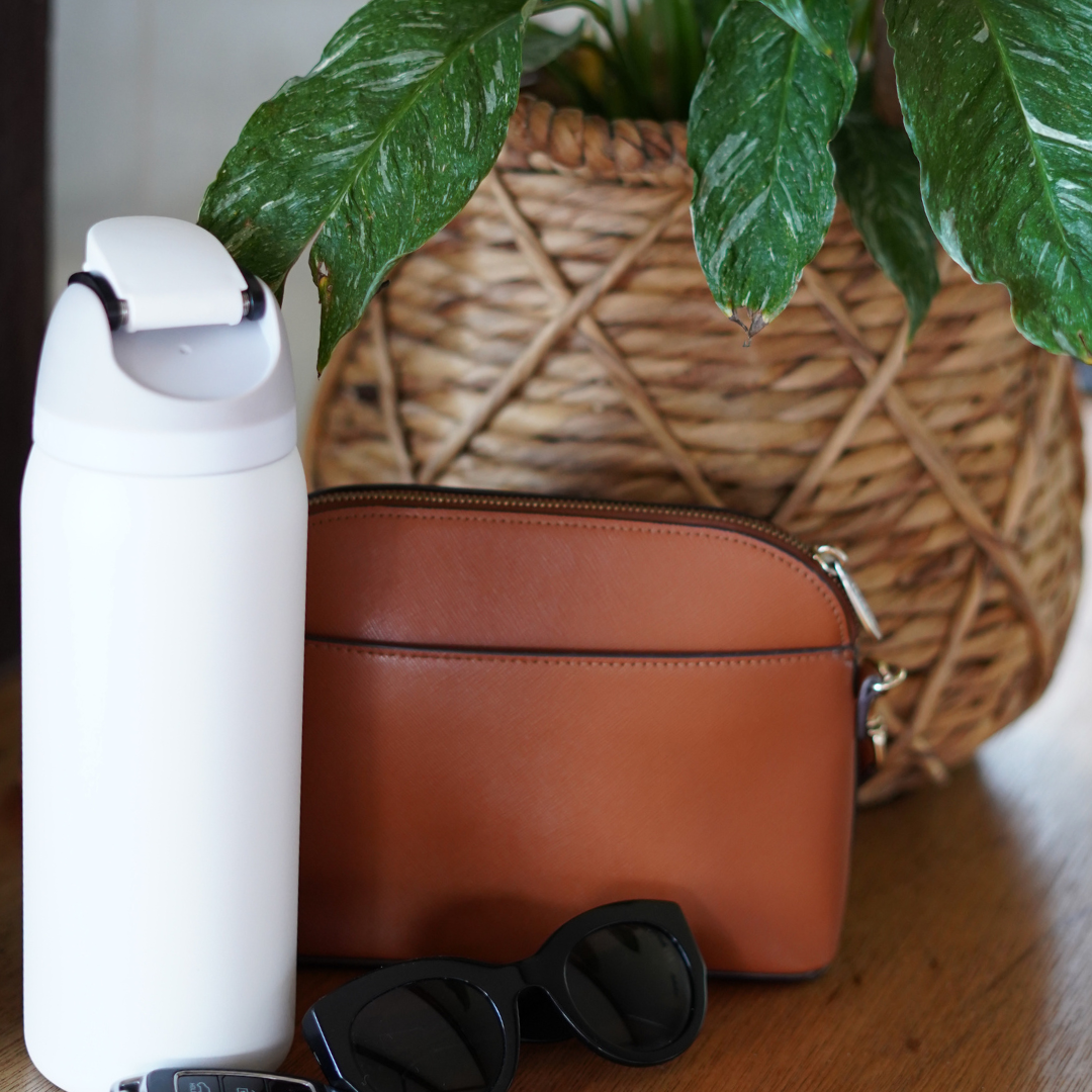 White Owala Reusable Water Bottle containing Access Filter Straw bag sunglasses keys on bench in front of plant