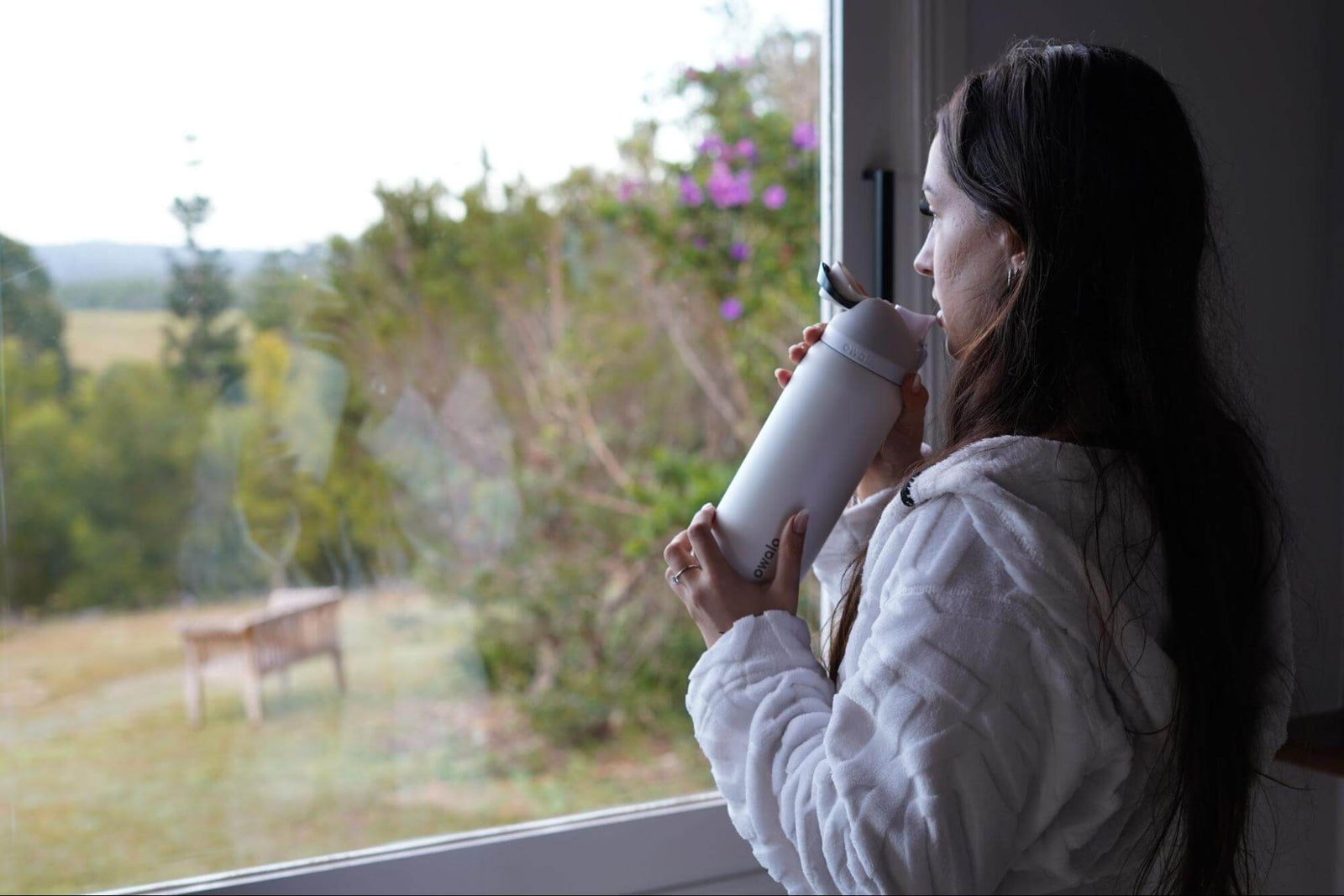 Female holding Owala reusable water bottle with filtered water inside looking out window to green garden