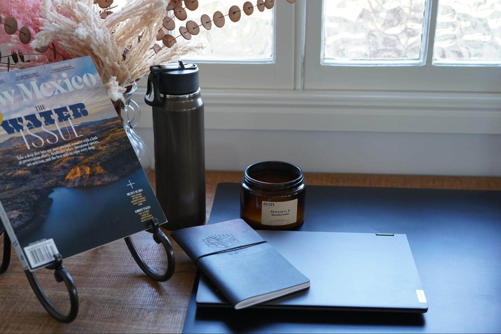 Hydro Flask water bottle with filtered water on desk with magazine laptop and candle