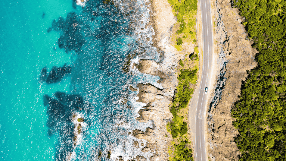 Car driving on coastal road next to water and bush